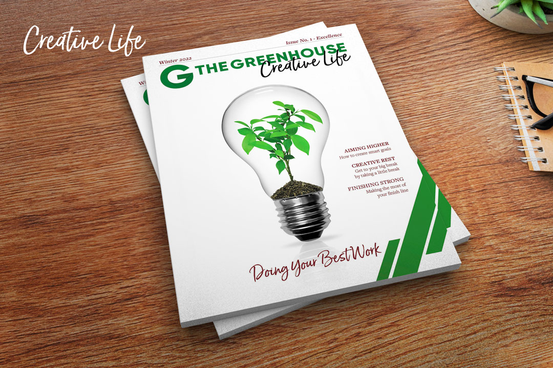 The Greenhouse - Creative Life Magazine stacked on a desktop with notebook and plant
